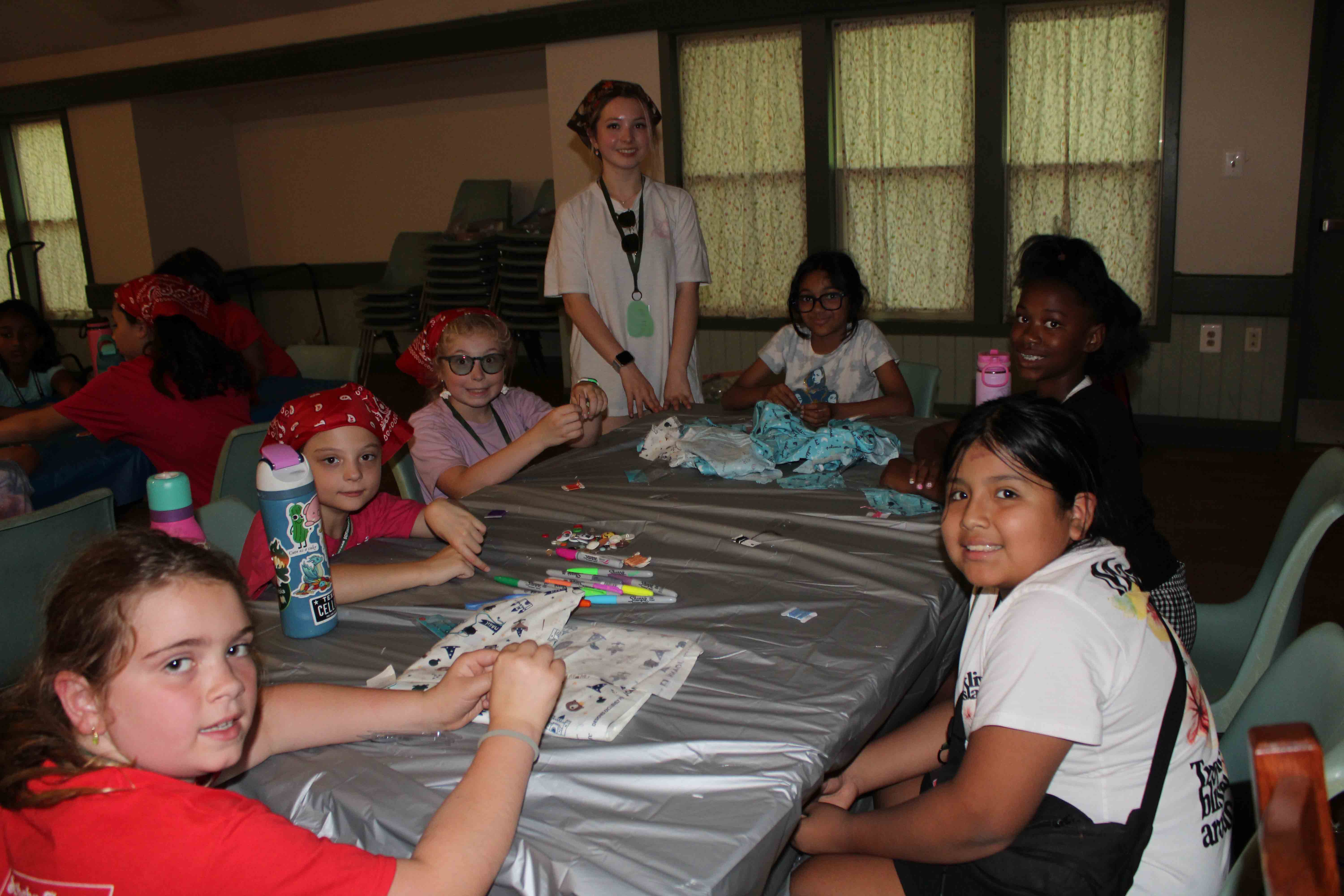 Campers in the Tornadoes 1 unit sitting at a table inside learning how to sew buttons onto custom cloth bags.
