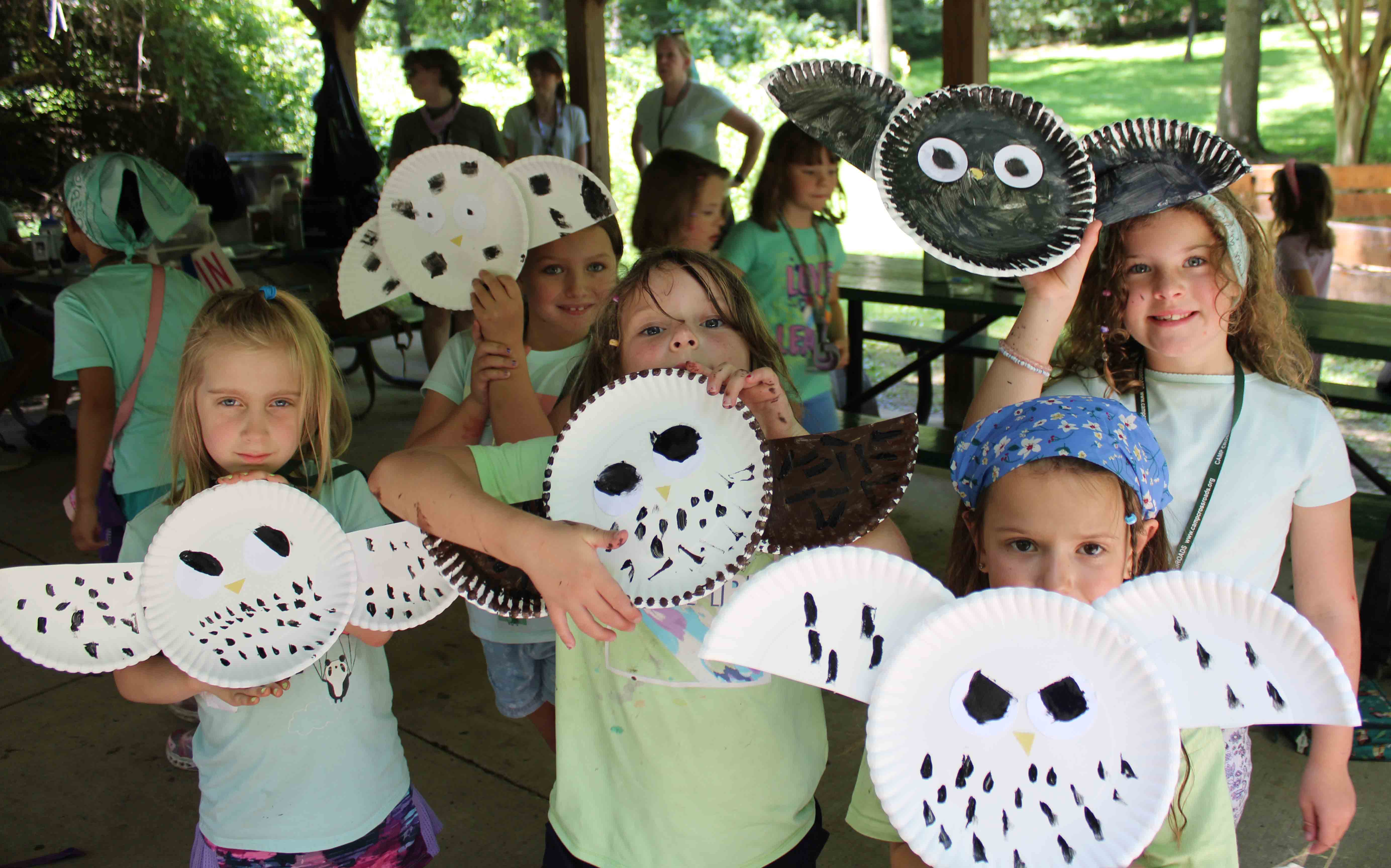 Campers from the Sunrays unit proudly showing off the paper plate owl crafts they made under a pavilion.