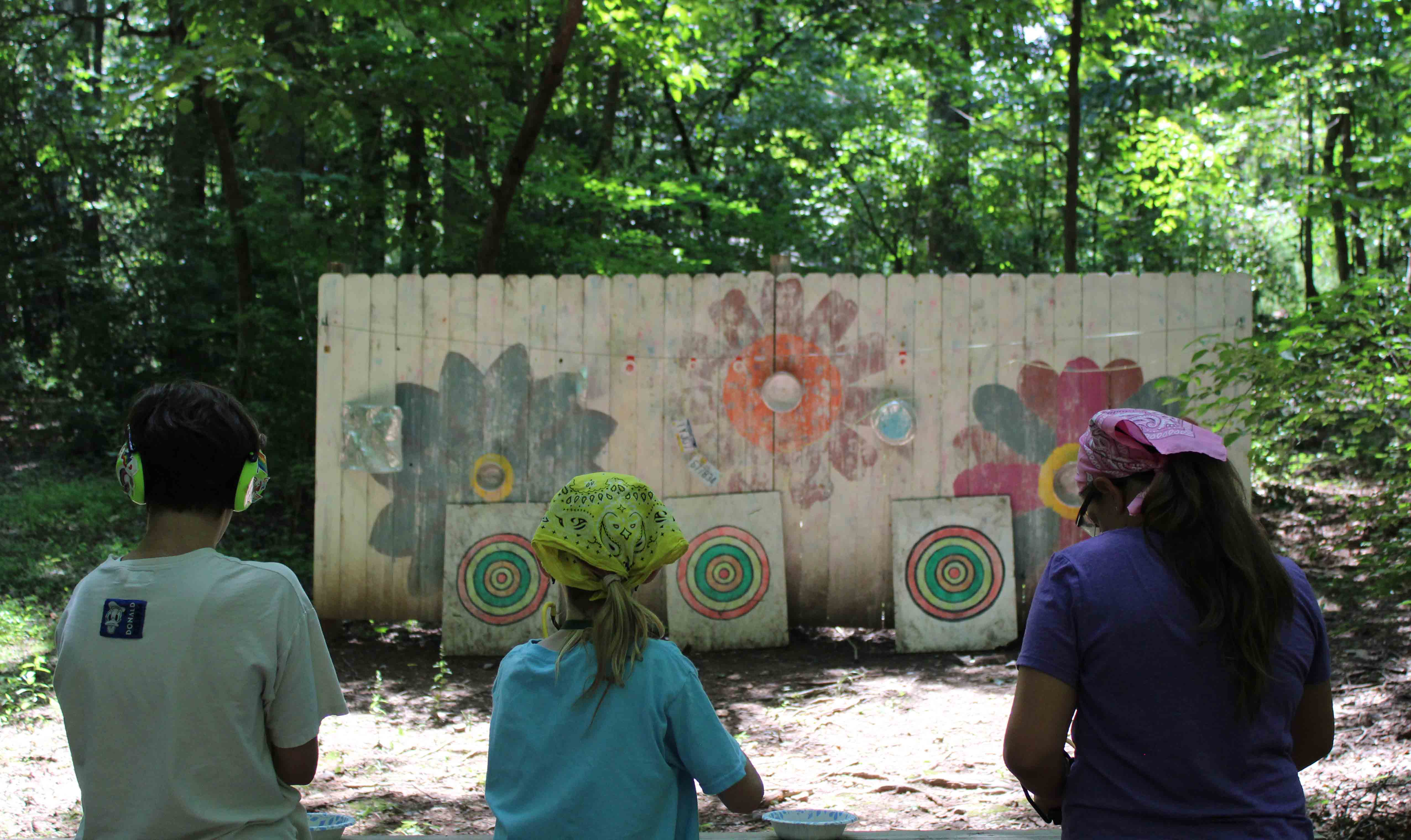 Three campers from the Catapults unit wearing bandanas while taking aim at target boards at the slingshot range.