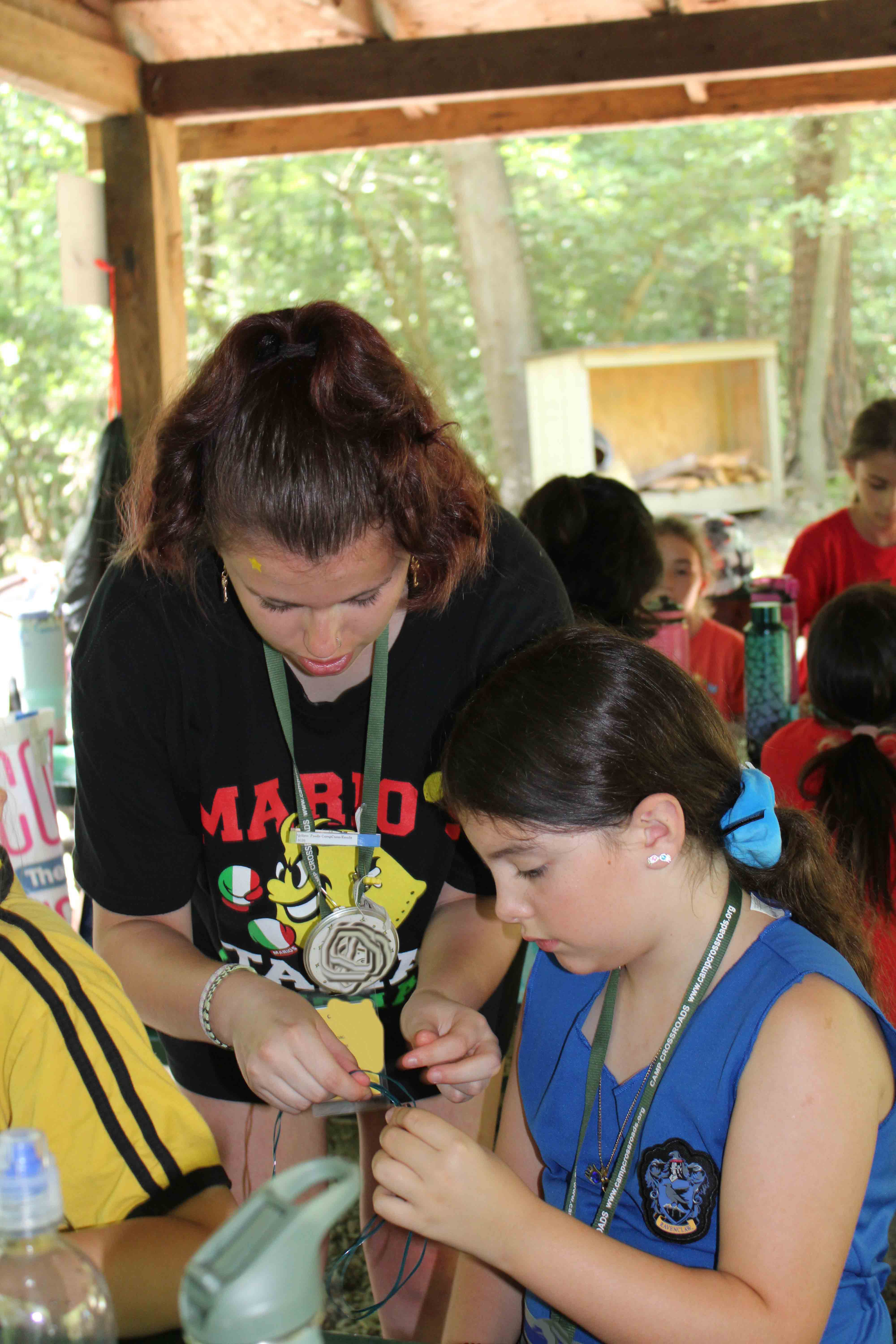 Campers gathered around a silver-clothed table inside a lodge working on custom crafts.